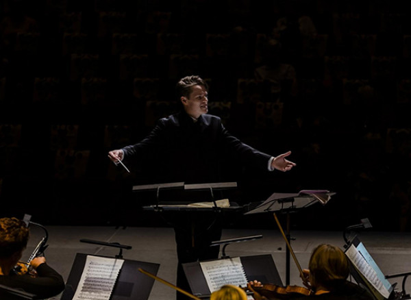 An image of Adam Hickox on stage conducting an orchestra