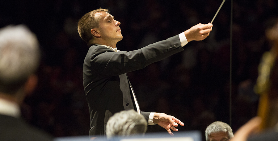 An image of a conductor, RPO Music Director Vasily Petrenko, holding a baton high with one hand wearing a black and white dress suit