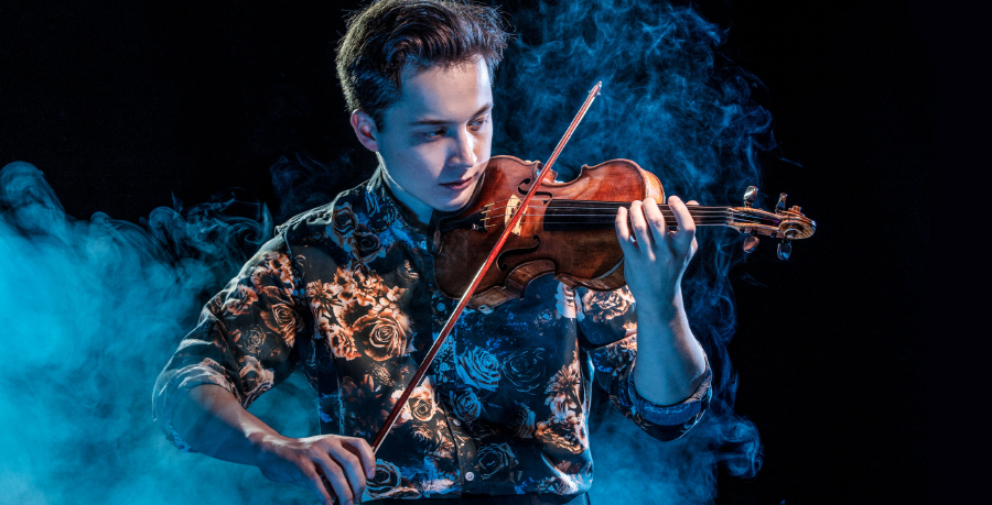 JOhan Dalene playing the violin in a burnished yellow floral shirt, and surrounded by dramatic blue smoke