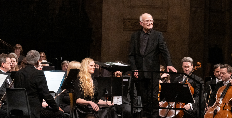 John Rutter smiling and facing the audience on the conductor's podium
