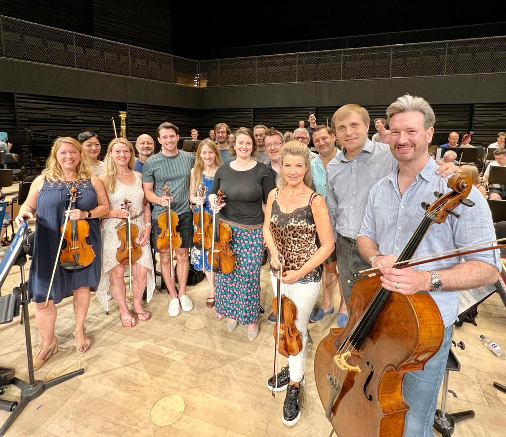 An image of Anne-Sophie Mutter with the string section of the RPO on stage in informal wear