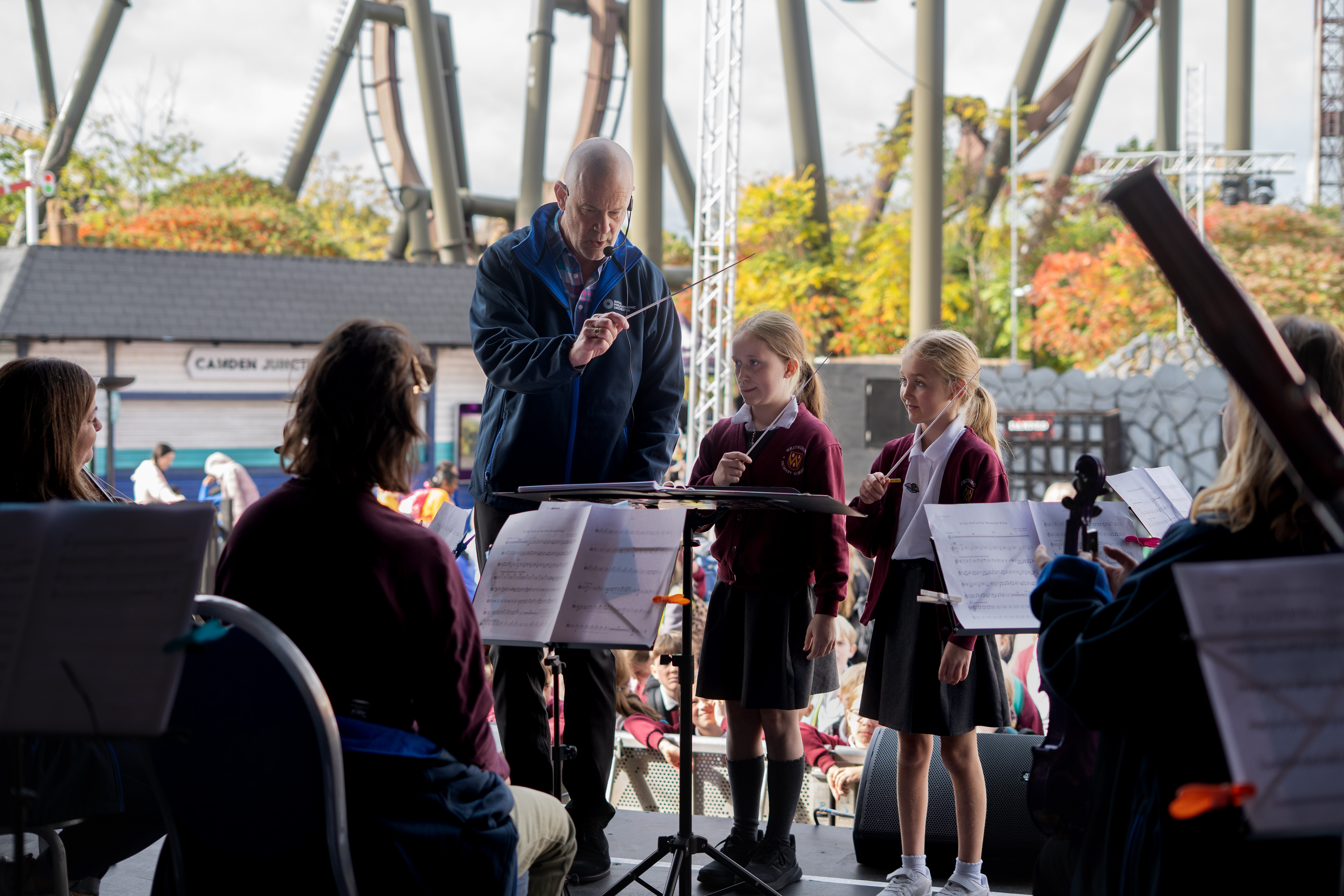 Participants conducting the Orchestra on stage, with roller coaster in the background