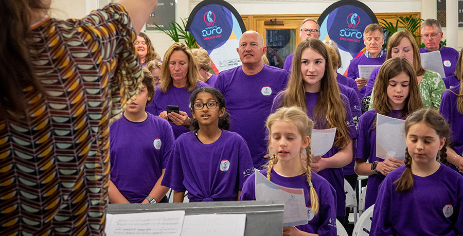 An image of a choir of young and older singers all wearing purple t-shirts