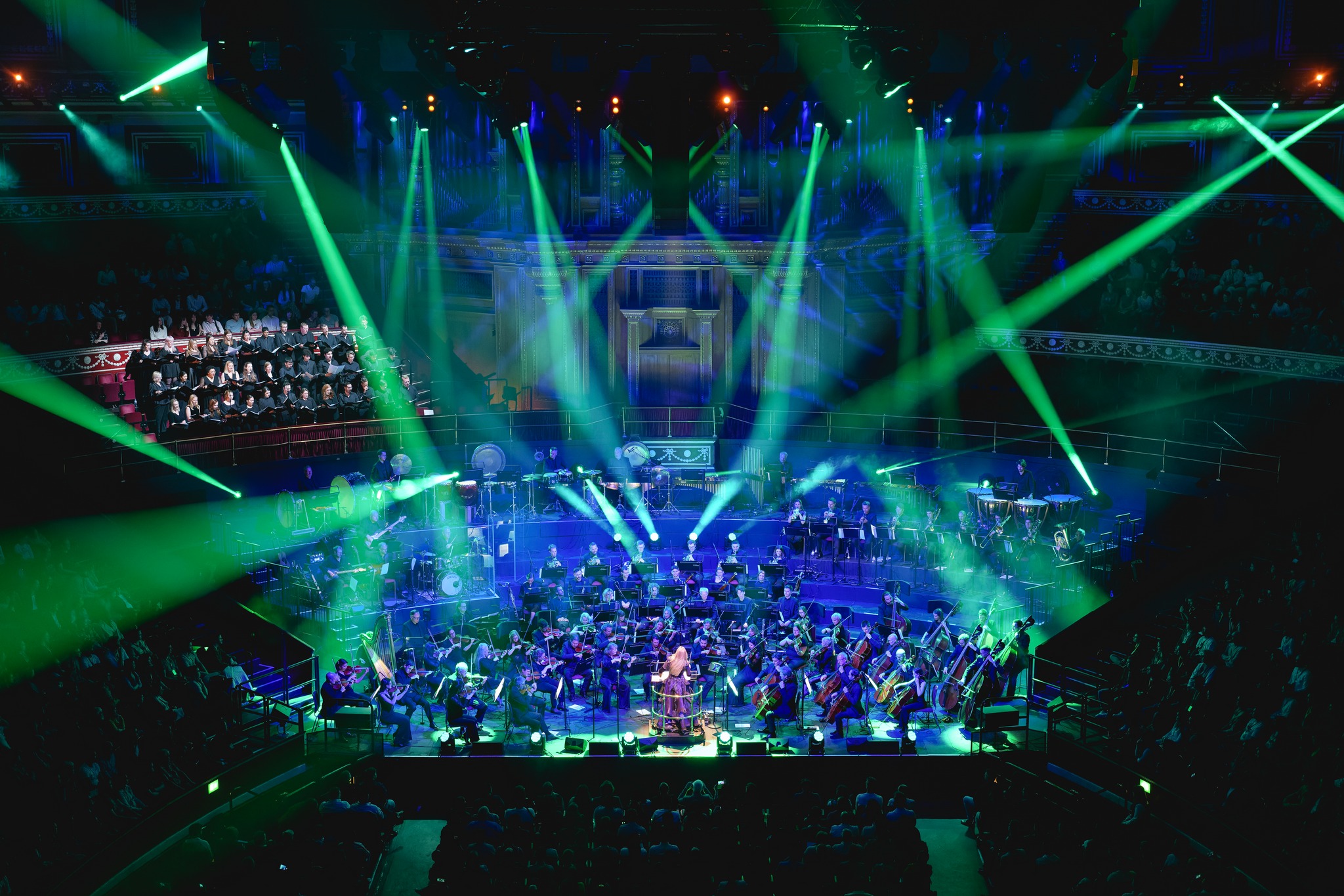 The Orchestra on stage at the Royal ALbert Hall with the Cantus Ensemble choir, with strong green beams lighting up the Hall