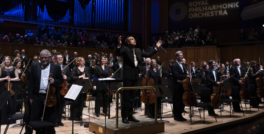 The Orchestra standing on stage at the Royal Festival Hall to receive applause, with Vasily Petrenko on the podium and raising his arms