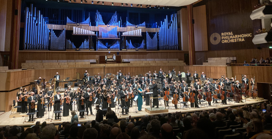 An image of the RPO on stage at Southbank Centre's Royal Festival Hall, where composer Dani Howard wearing a green dress is applauded by the audience