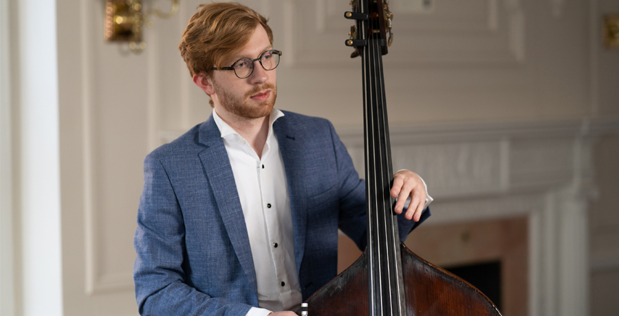 Jason Henery in a white shirt and blue suit jacket holding his double bass