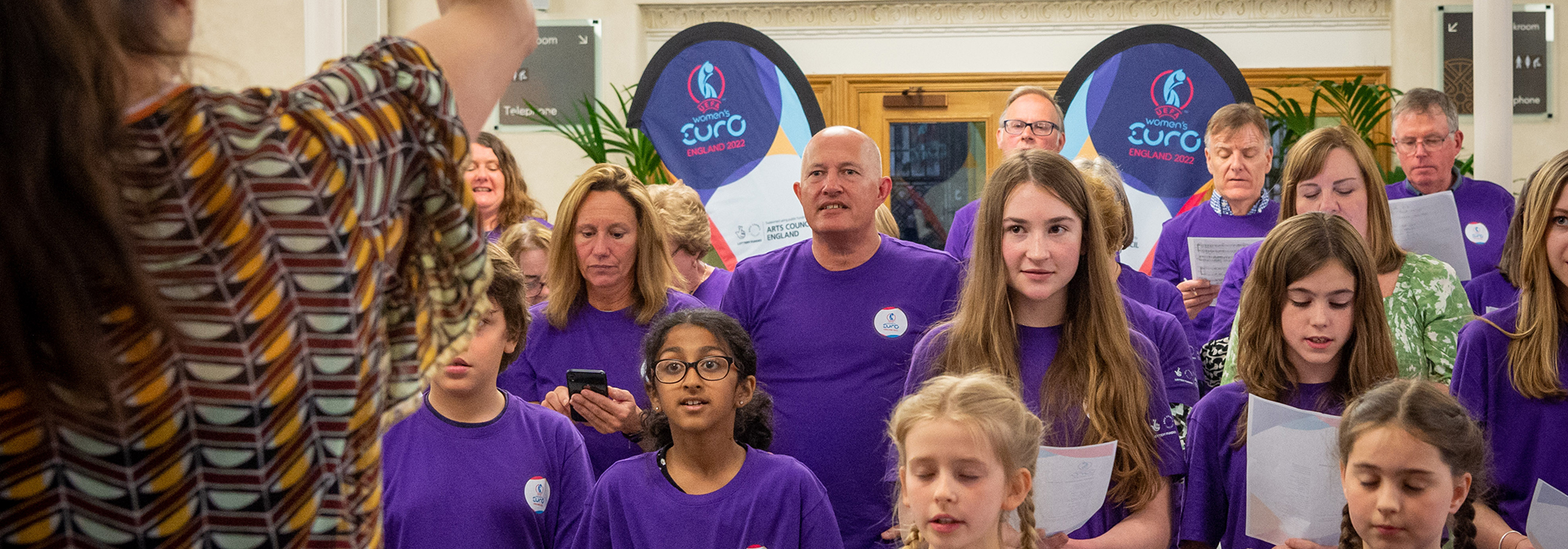 An image of a choir of young and old singers. All wearing purple t-shirts