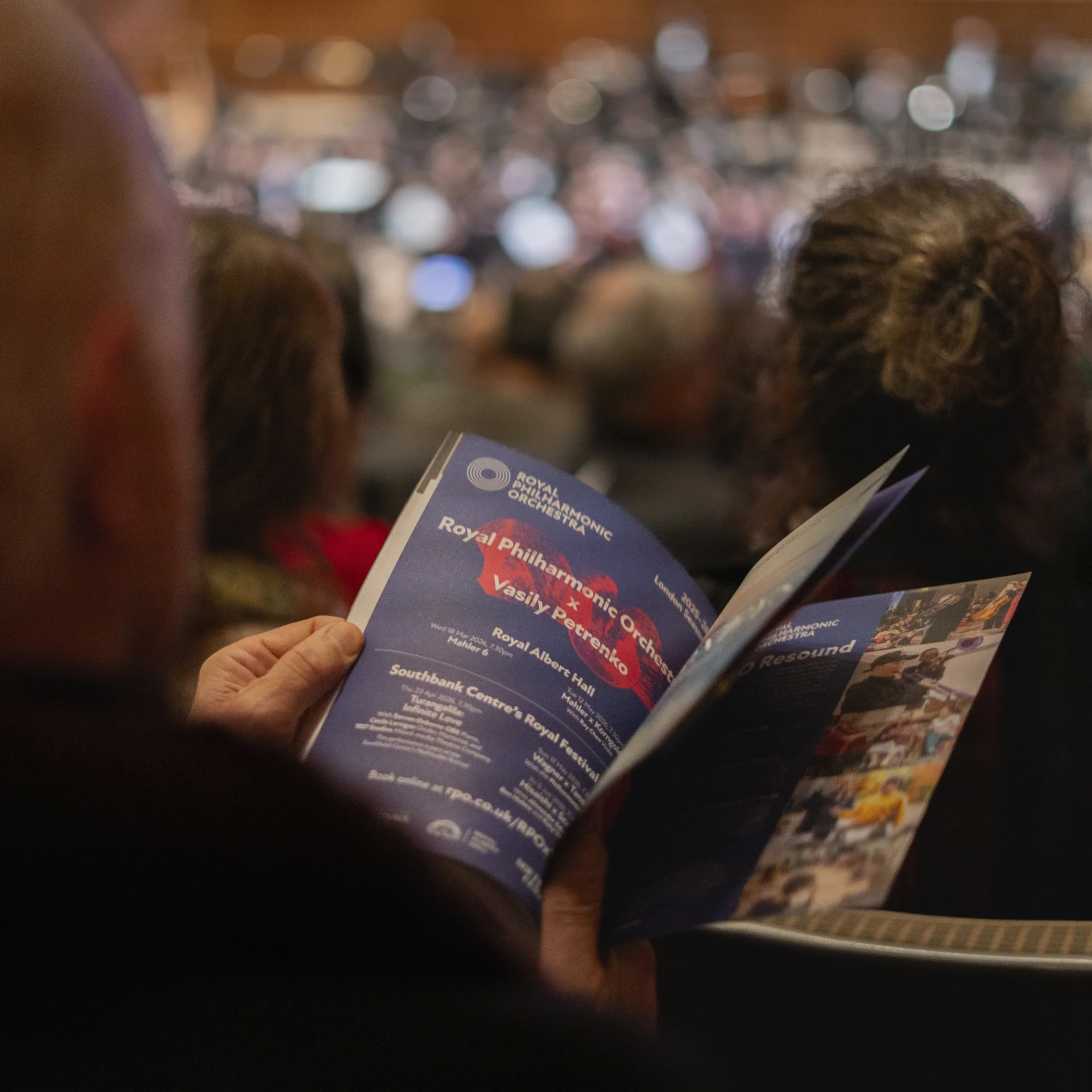 A man seated in the audience flicking through a programme