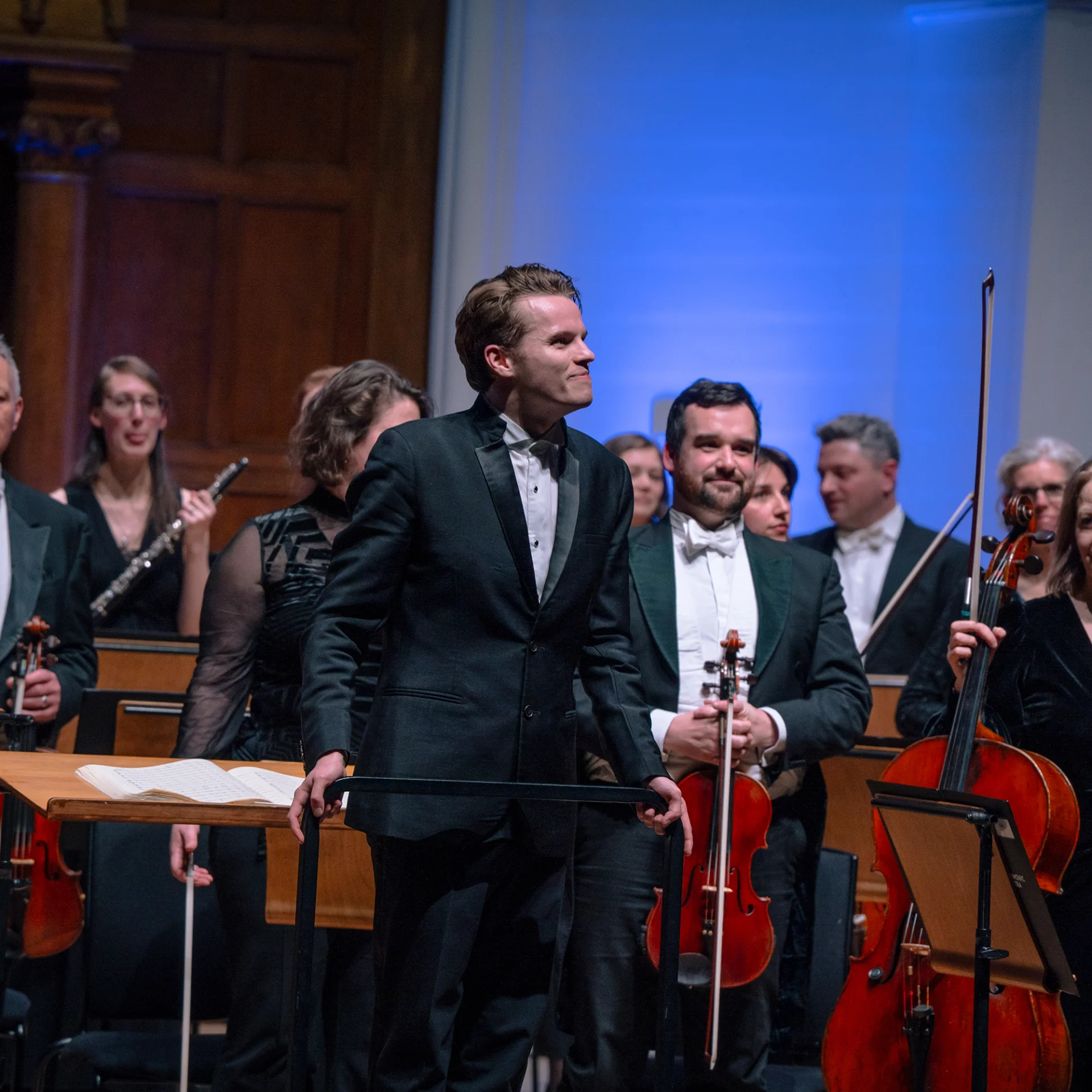 Adam Hickox standing on the podium of Cadogan Hall as he and the Orchestra receive applause