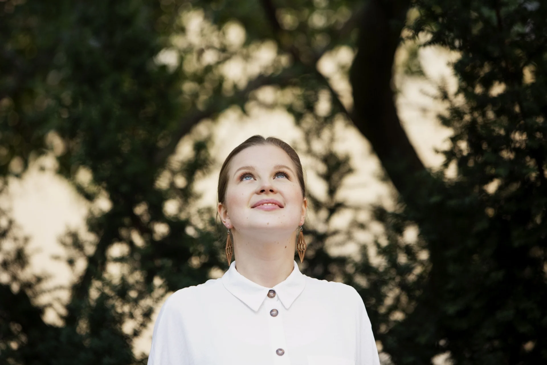 Emilia Hoving is in a white shirt, she stands in front of a tree canopy and she is looking upwards