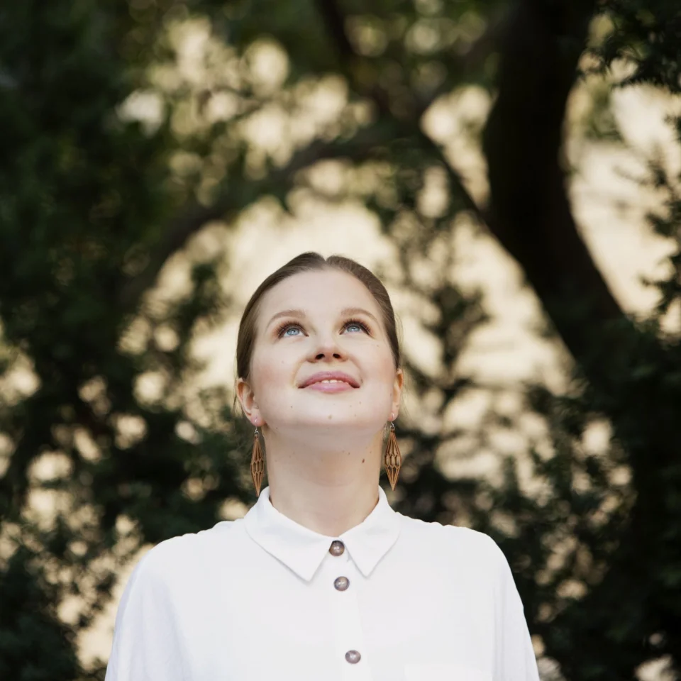 Emilia Hoving is in a white shirt, she stands in front of a tree canopy and she is looking upwards