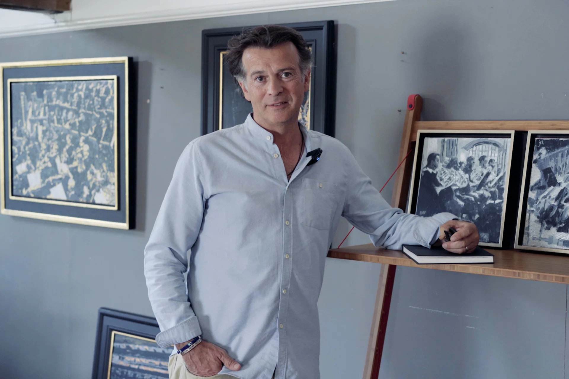Jeremy Houghton posing by paintings of the Orchestra in his studio gallery