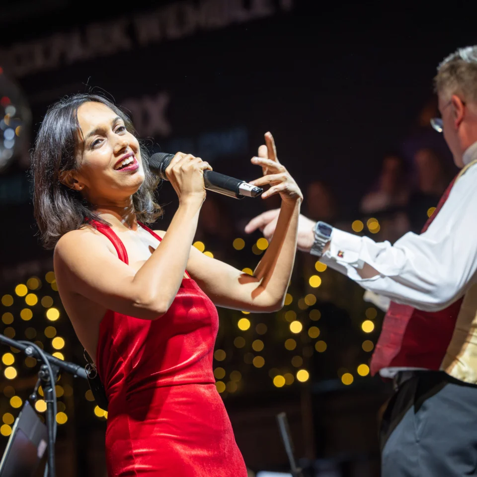 Vocalist Sumudu Jayatilaka singing into a microphone with shining lights in the background.