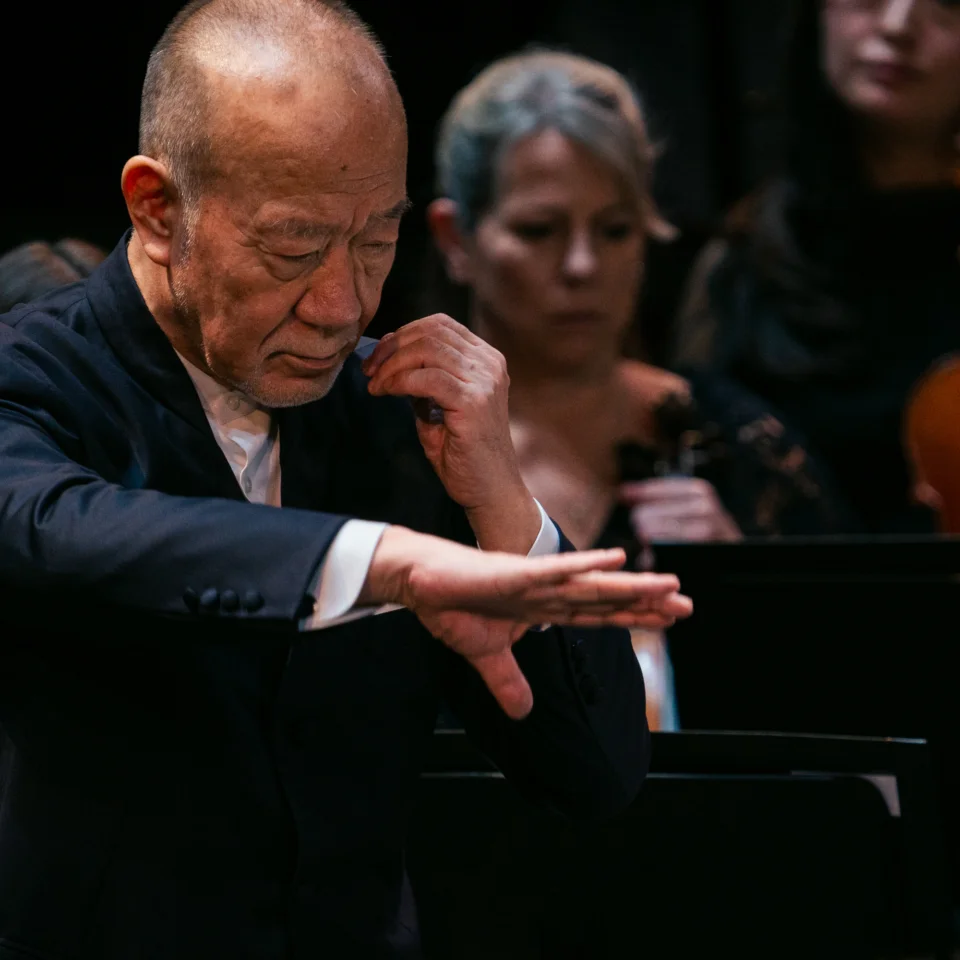 Joe Hisaishi conducting with his right palm spread out and his left hard held towards his face