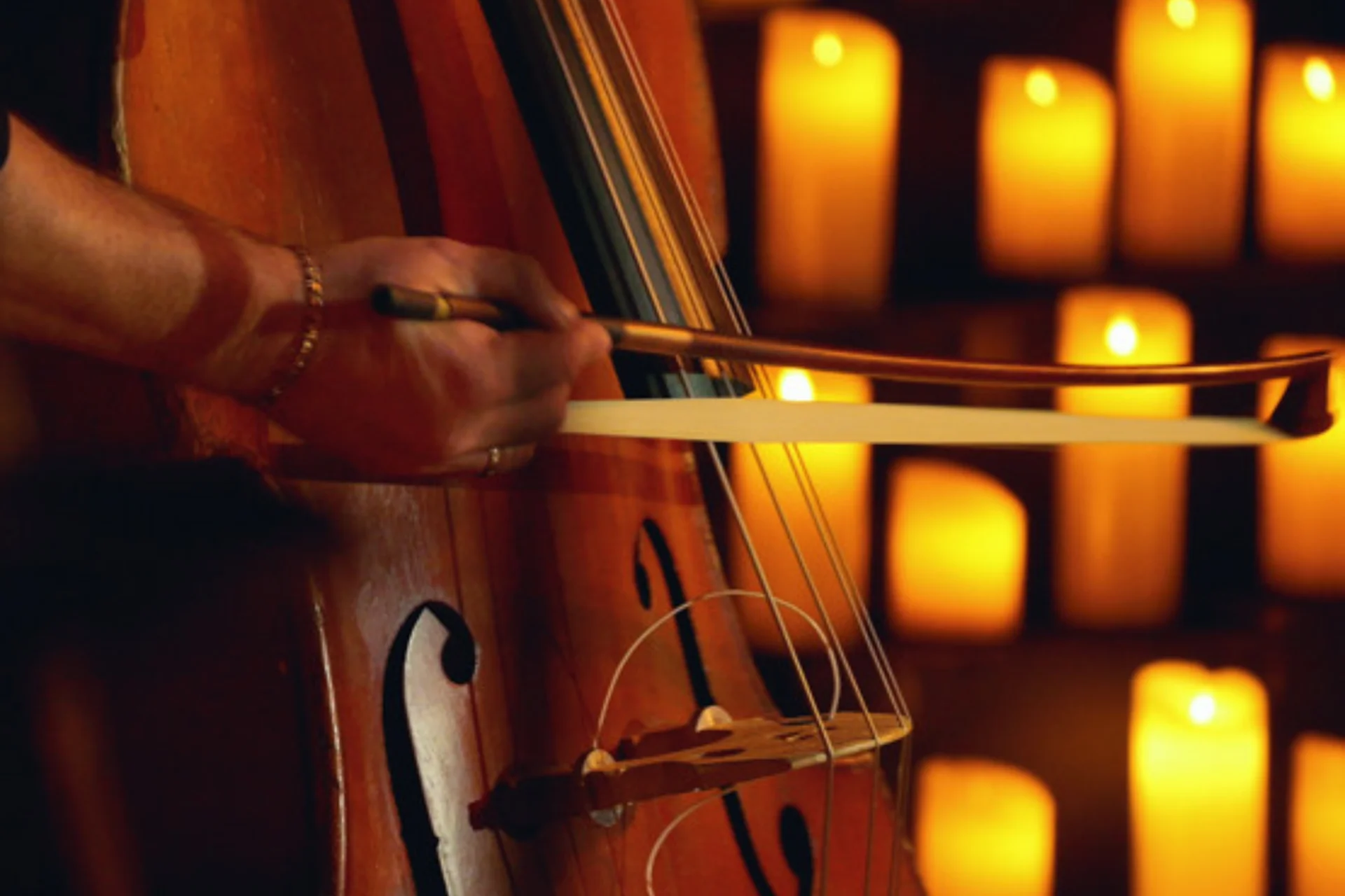 A cello is played in front of candles