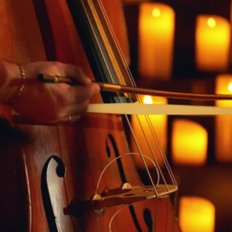A cello is played in front of candles