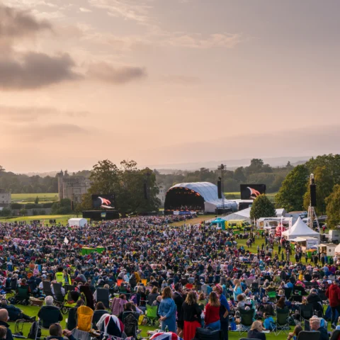 Crowds at Leeds Castle watching the outdoor stage as sunset approaches