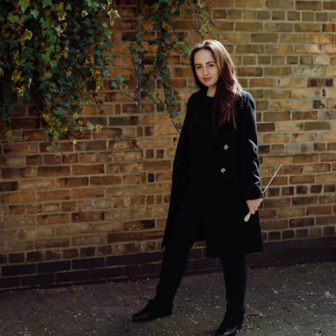 Conductor Olivia Clarke stand with baton in hand, looking into the camera