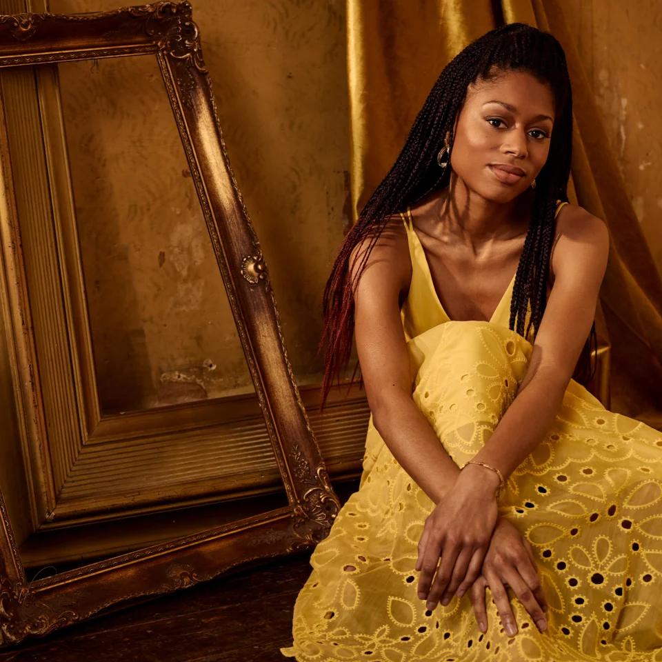 Isata Kanneh-Mason seated in yellow dress in front of empty gold mirror