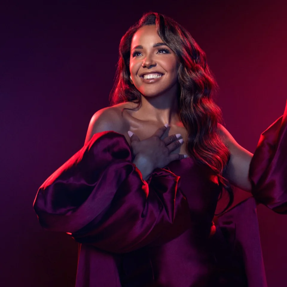 A photo of Shanay Holmes under theatre-style lighting and smiling