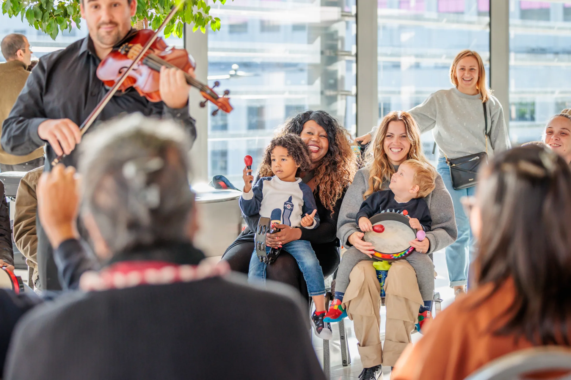 Round children with their parents sitting and playing percussion in a circle with an RPO violist playing near them