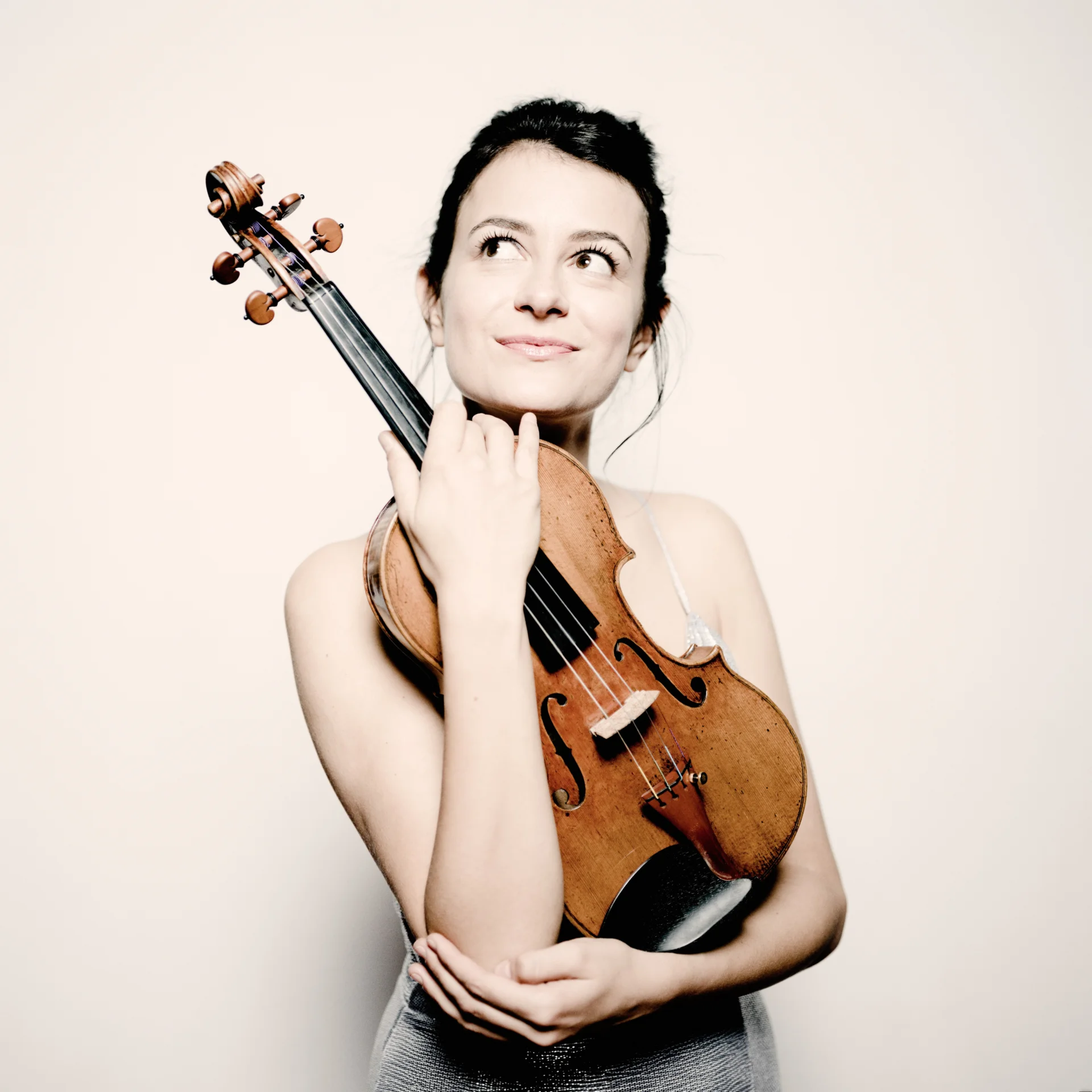 A photo of Liya Petrova looking upwards away from the camera, holding her violin.