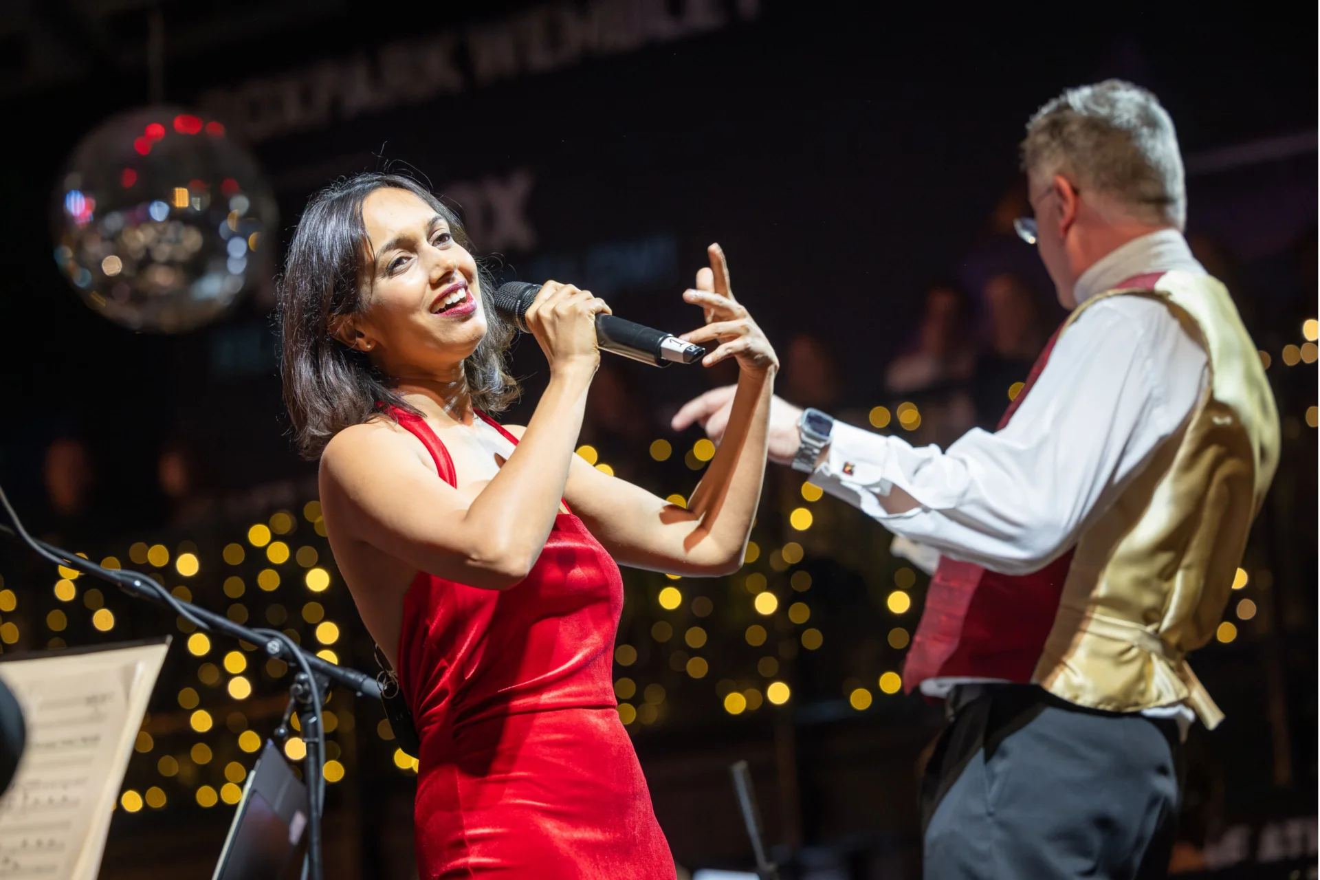 Vocalist Sumudu Jayatilaka singing into a microphone with shining lights in the background.