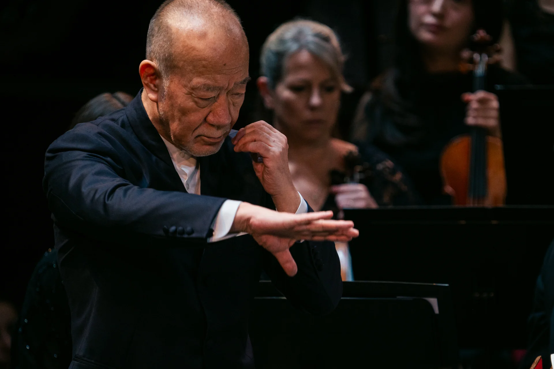 Joe Hisaishi conducting with his right palm spread out and his left hard held towards his face