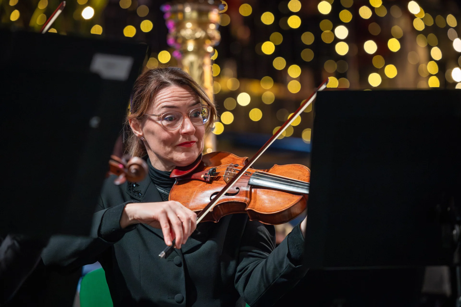 An RPO violinist playing on stage with a harp and sparkly Christmas lights behind her