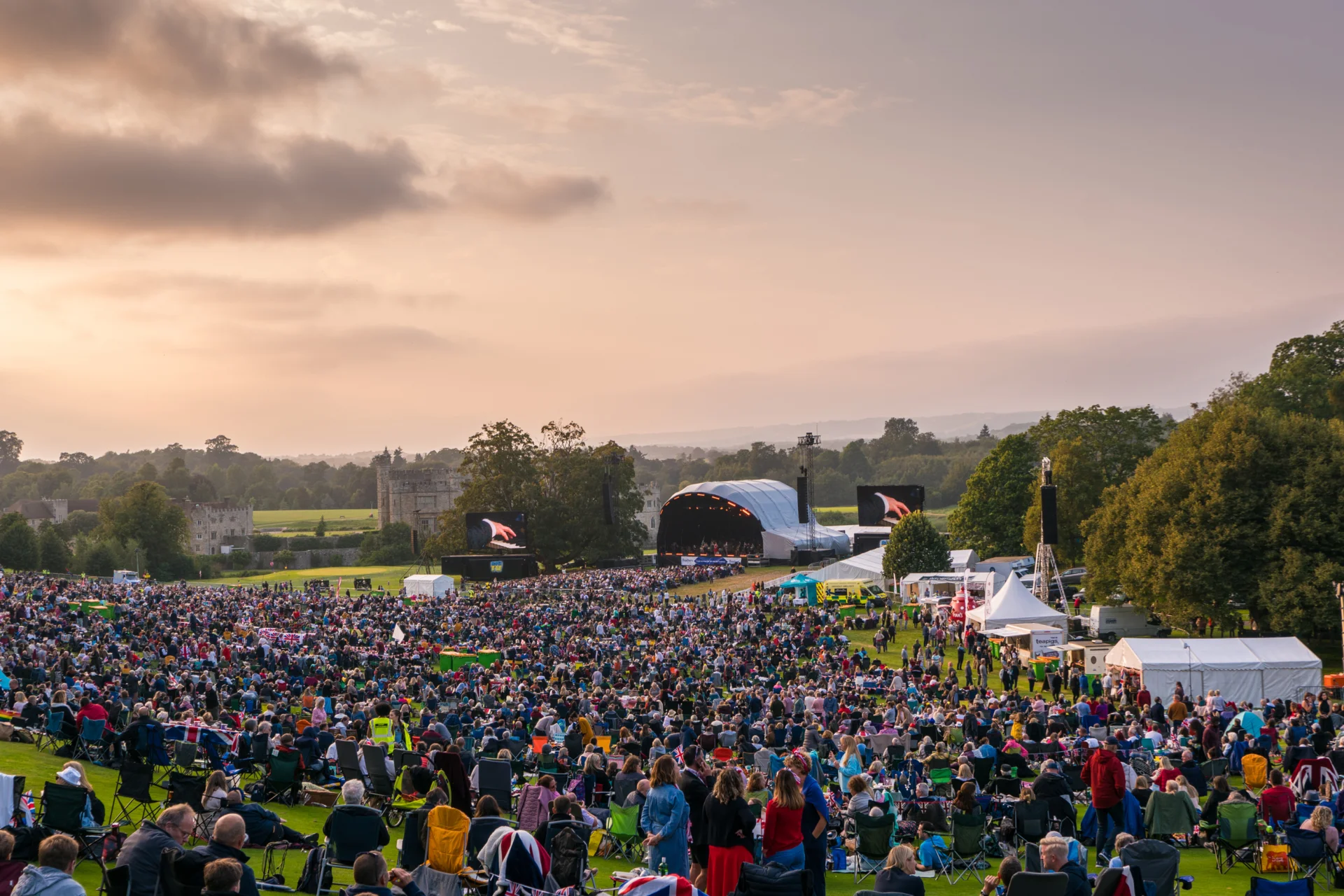 Crowds at Leeds Castle watching the outdoor stage as sunset approaches