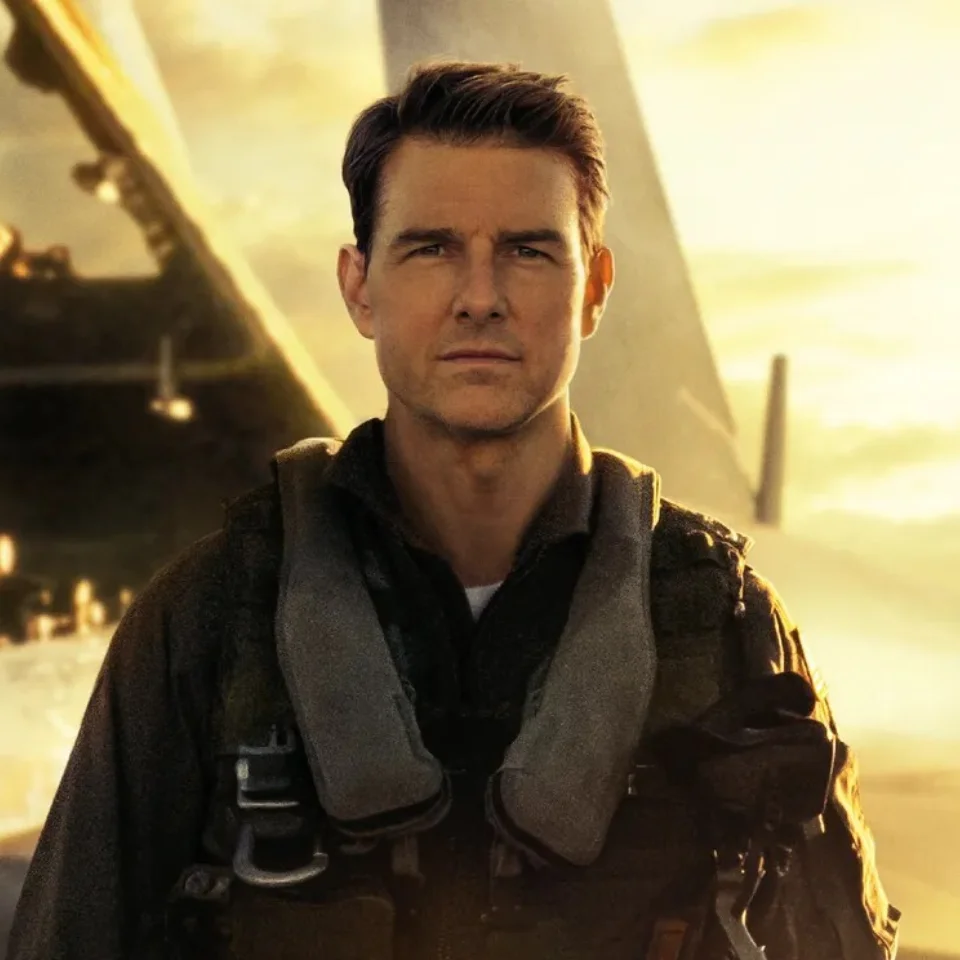 Tom Cruise in character as 'Maverick' standing in front of a fighter jet in the film 'Top Gun'.
