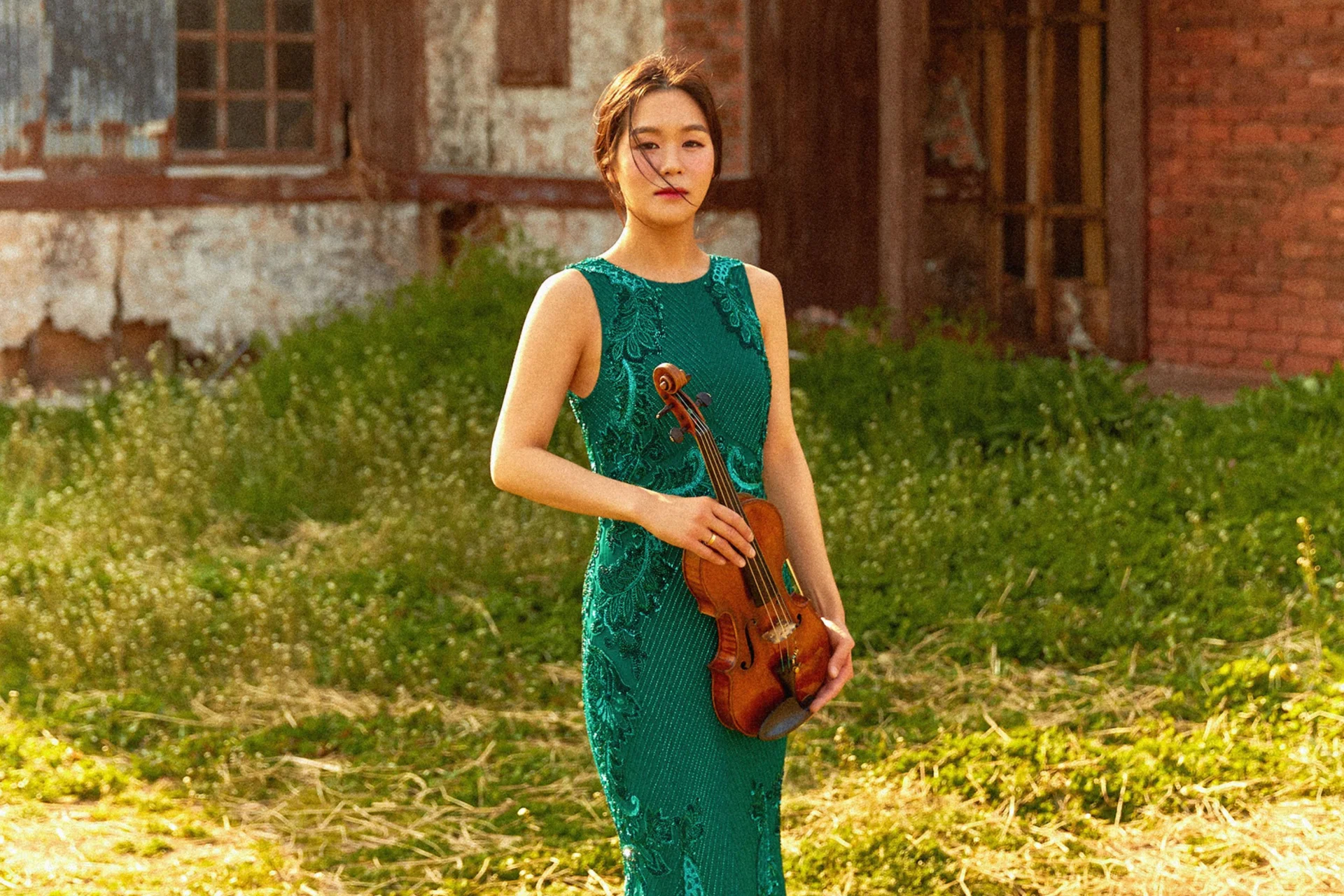 Esther Yoo stands in a field holding her violin