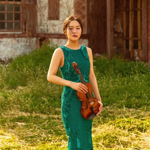 Esther Yoo stands in a field holding her violin