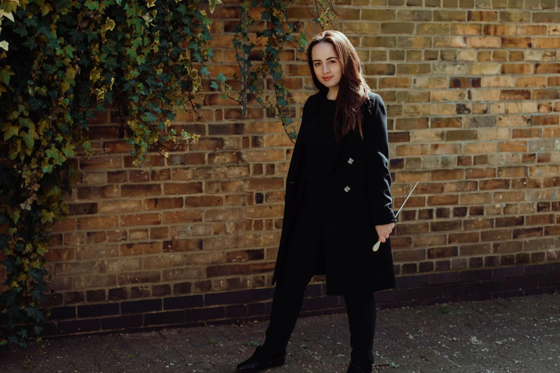 Conductor Olivia Clarke stand with baton in hand, looking into the camera
