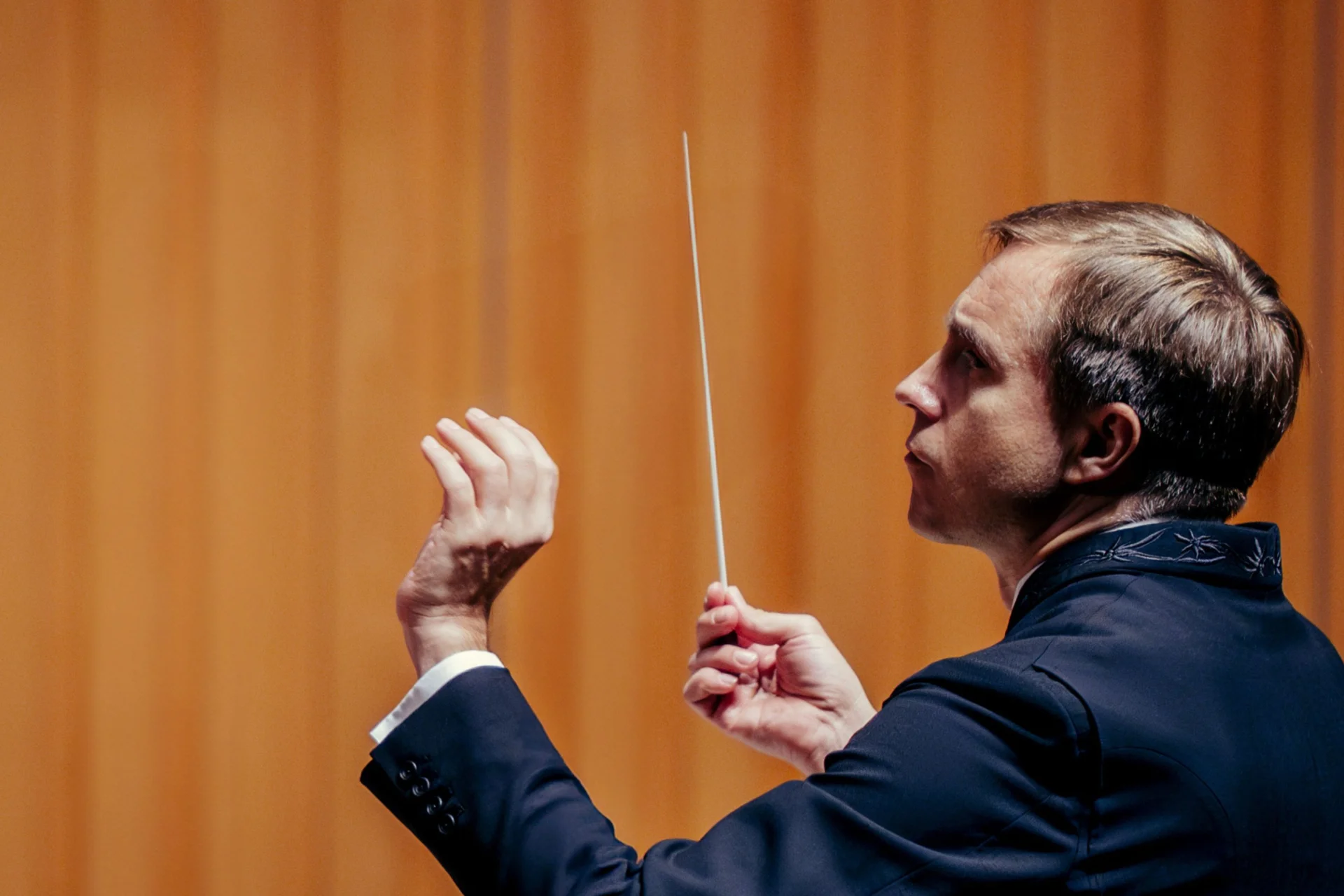 Music Director Vasily Petrenko conducting in front of a bright orange background
