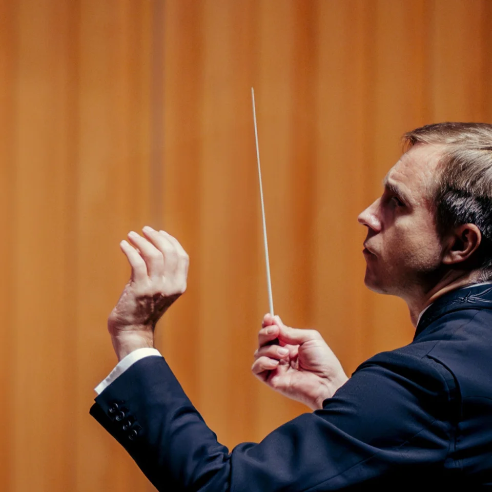 Music Director Vasily Petrenko conducting in front of a bright orange background