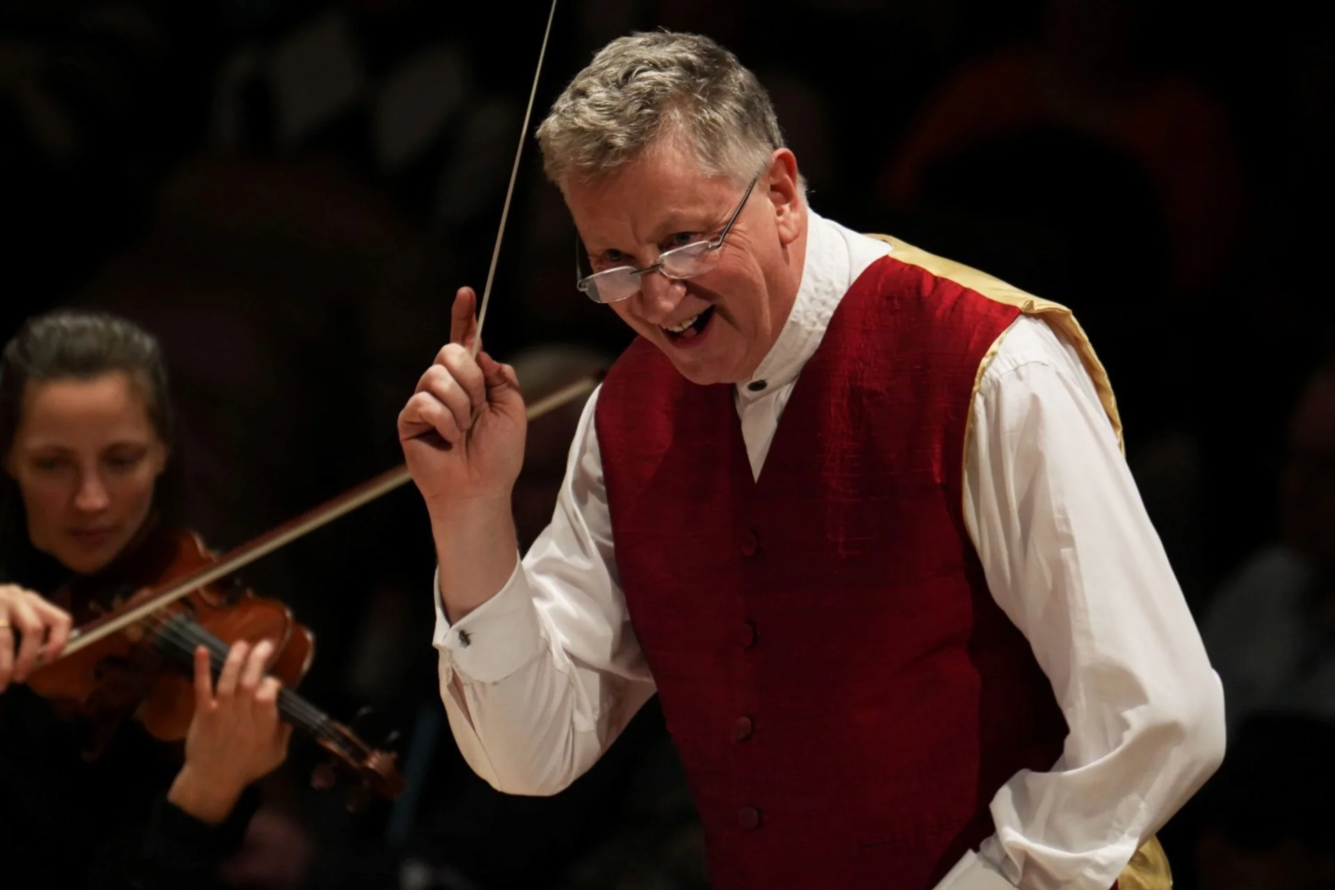 Conductor Steven Bell on stage with baton in hand, smiling
