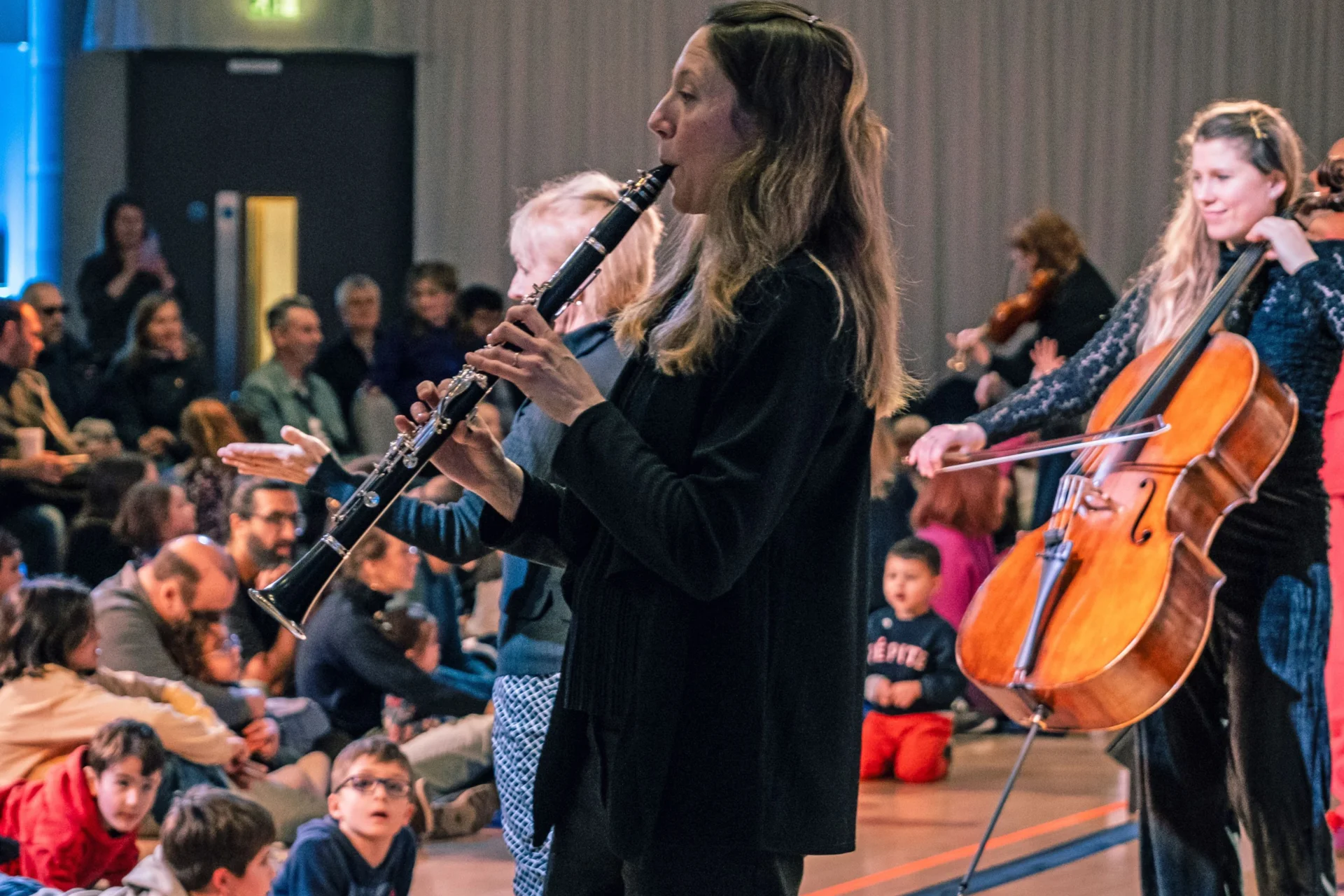 Royal Philharmonic Orchestra musicians play their instruments at a relaxed performance, integrating with the audience, some of which are sitting on floor mats