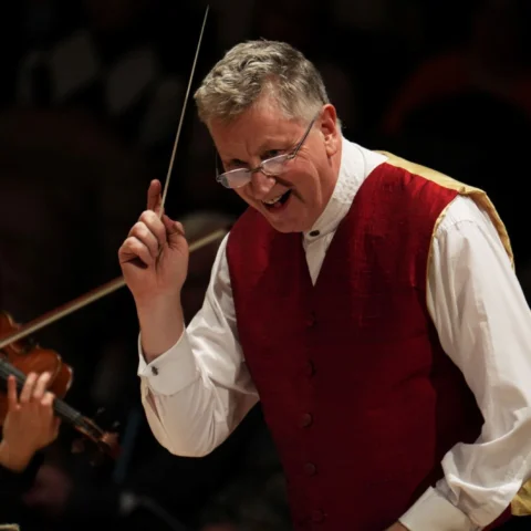 Conductor Steven Bell on stage with baton in hand, smiling