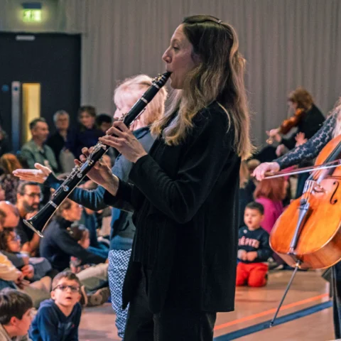 Royal Philharmonic Orchestra musicians play their instruments at a relaxed performance, integrating with the audience, some of which are sitting on floor mats