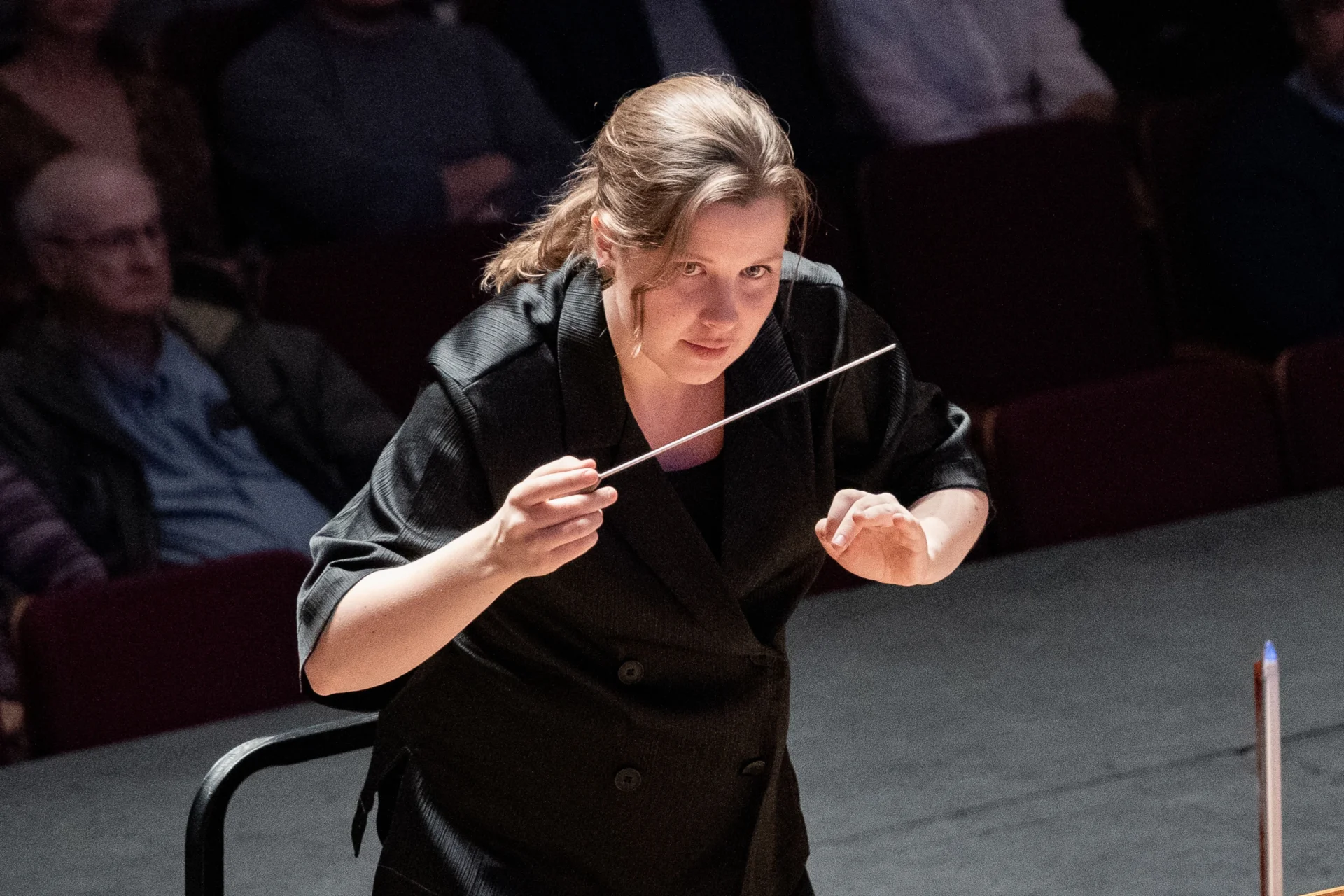 Conductor Emilia Hoving leans in towards the orchestra, baton in hand
