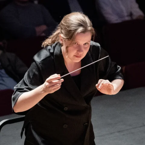Conductor Emilia Hoving leans in towards the orchestra, baton in hand