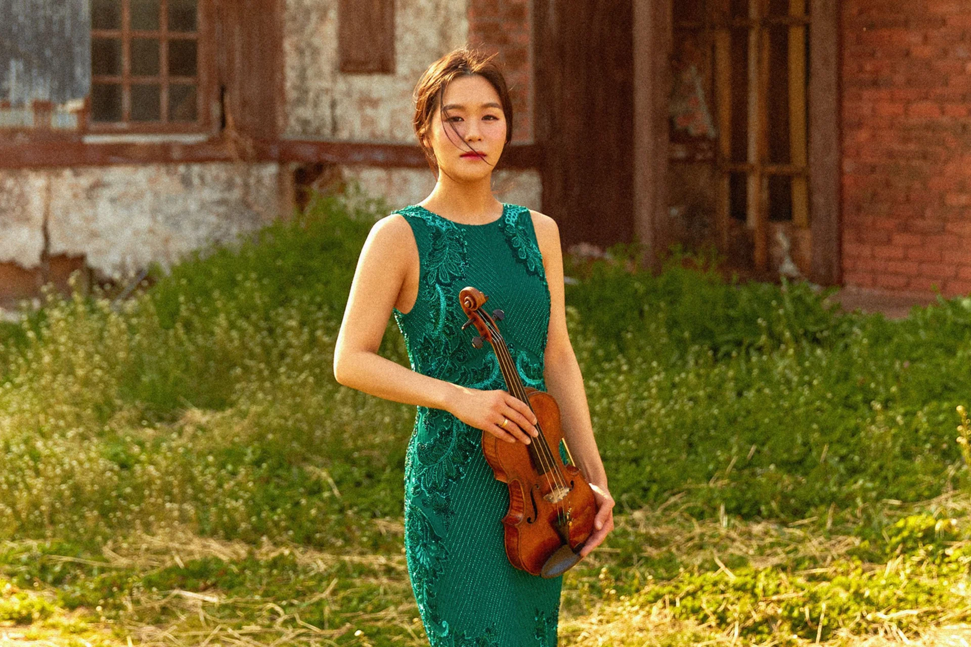 Esther Yoo stands holding her violin in a sunny field