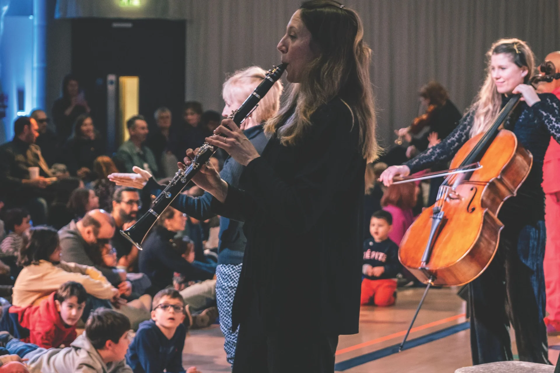 A clarinet player and a cellist perform at a Relaxed Performance, looking out onto the audience, some of whom are sitting on mats on the floor