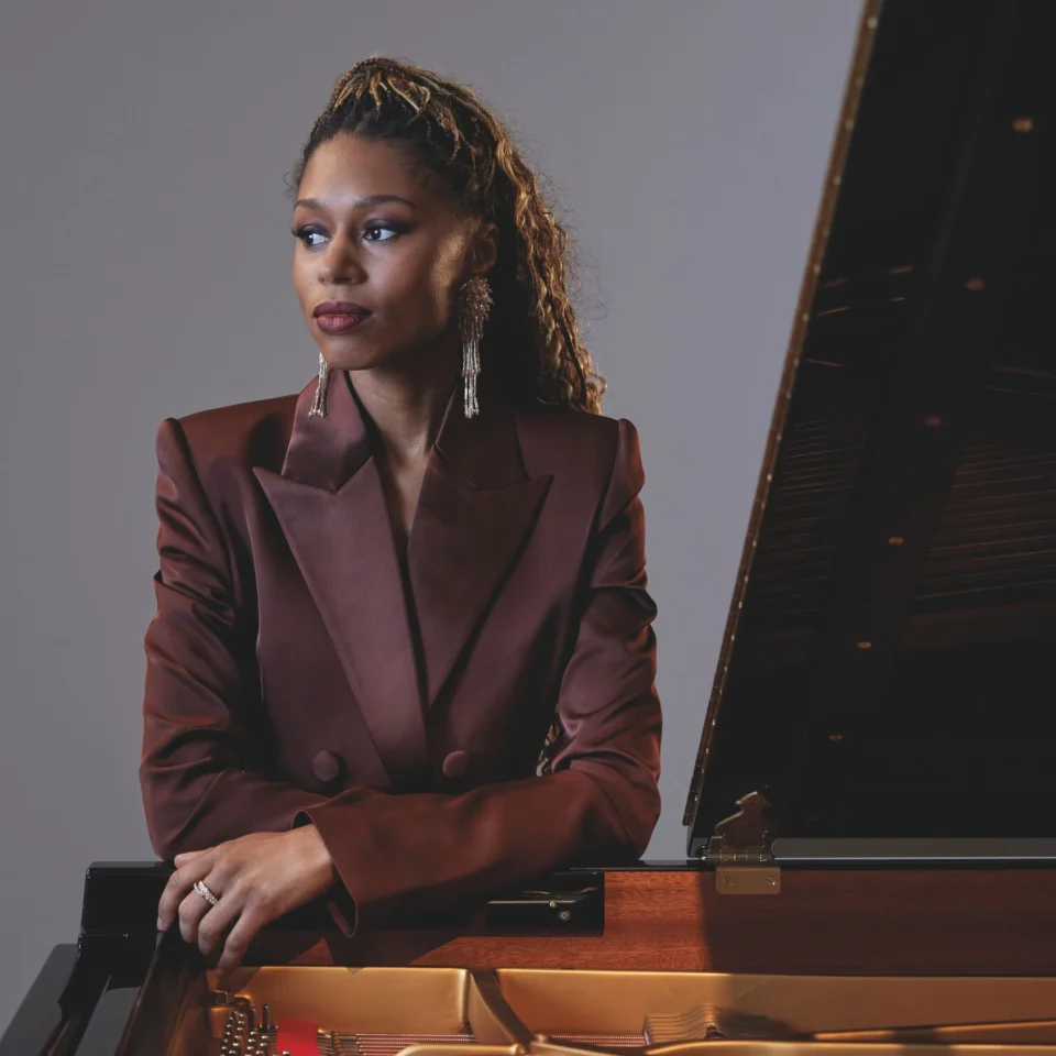 Isata Kanneh Mason stands leaning on a piano