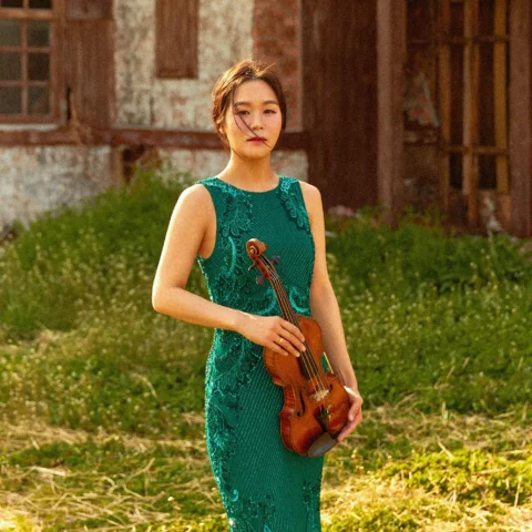 Esther Yoo stands holding her violin in a sunny field