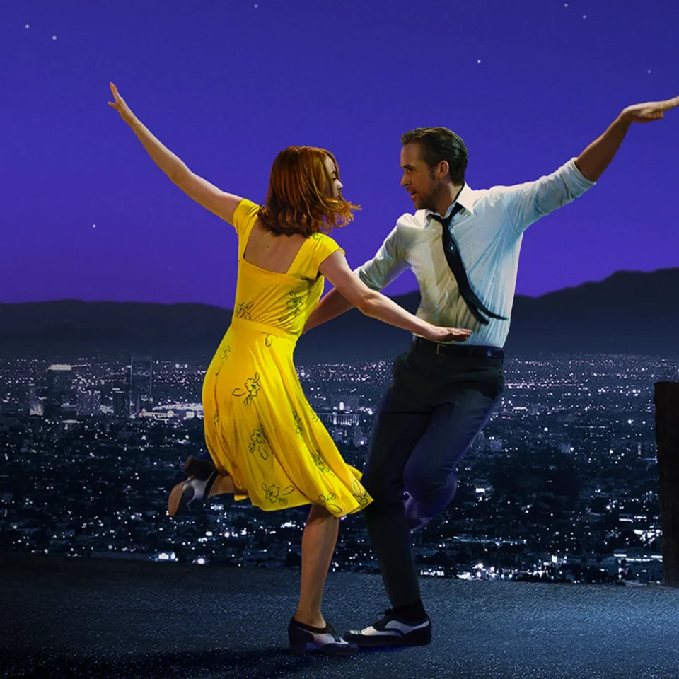 Two dancers in front of the LA skyline, one woman in a yellow dress and one man in a suit.