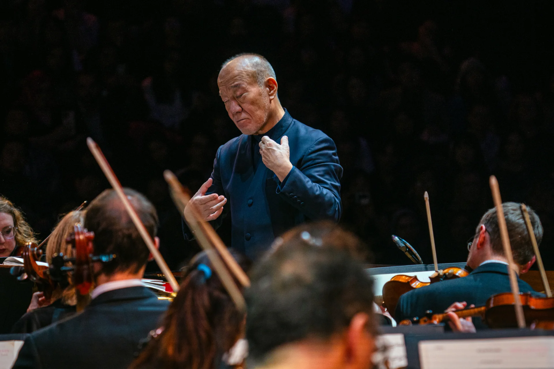 Joe Hisaishi conducting the Orchestra. His hands and held towards himself and his eyes are closed