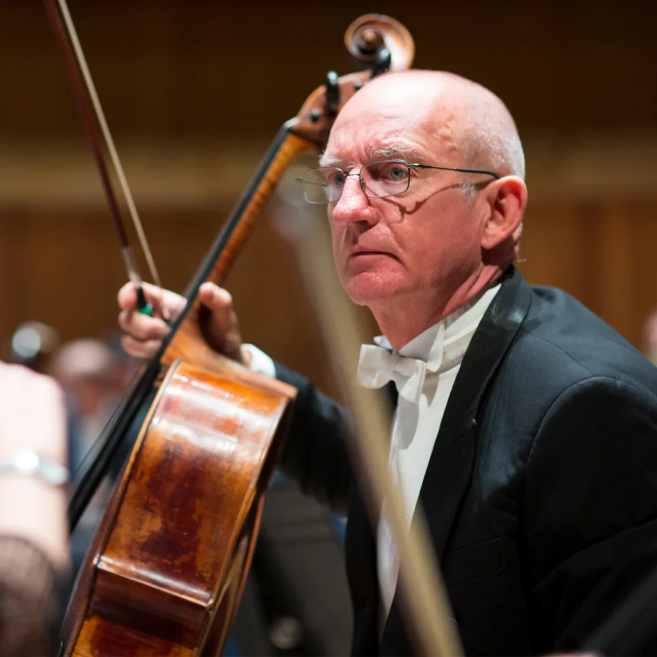 Cellist Bill Heggart sitting and holding his cello in rehearsal